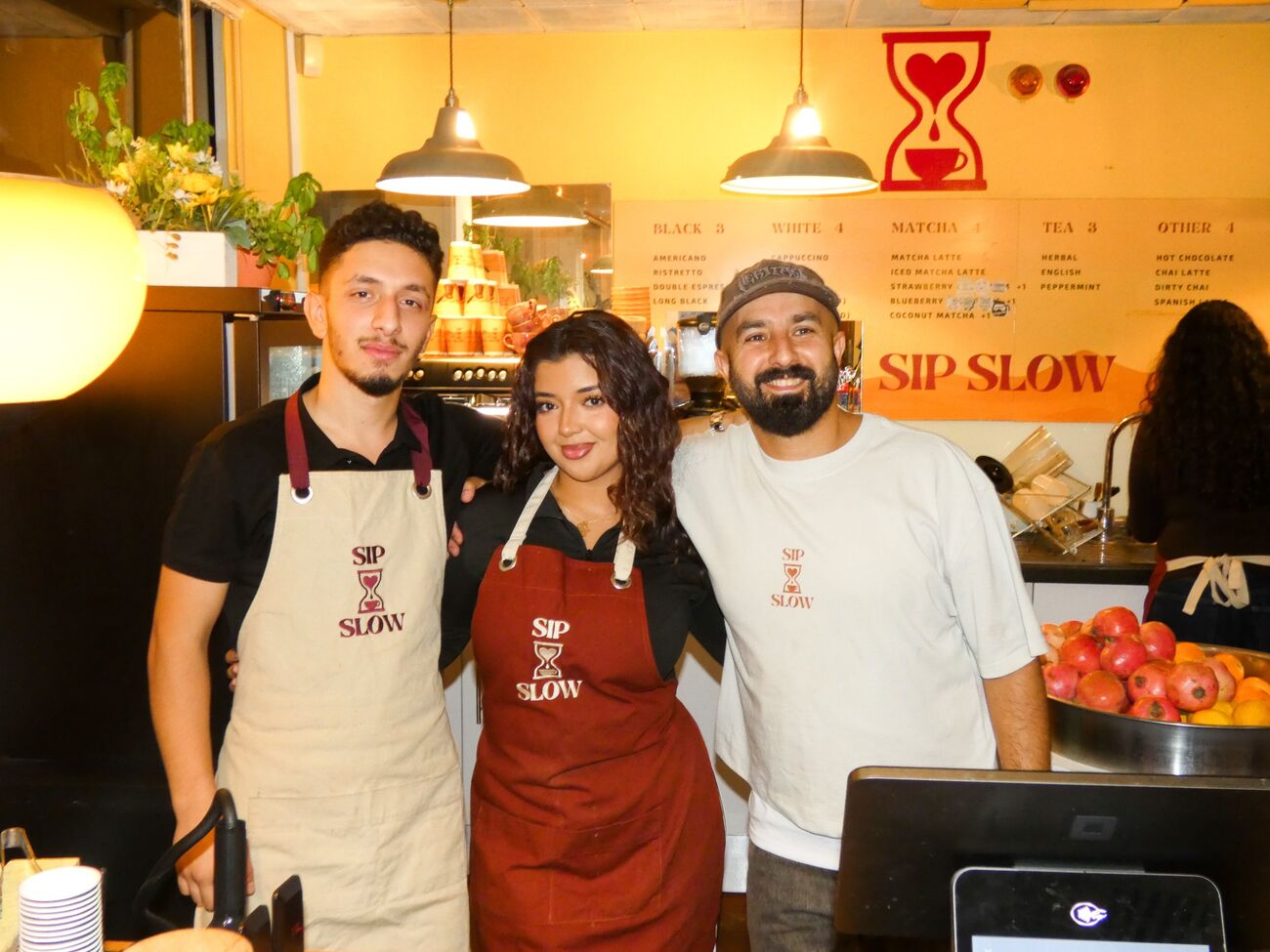 Three Sip Slow baristas in branded aprons behind the counter